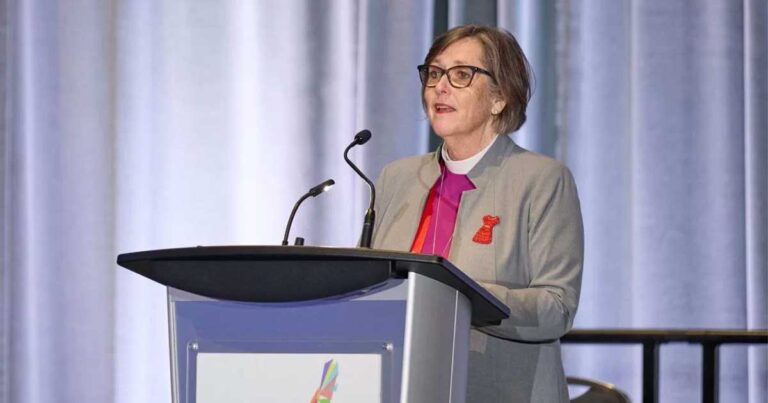 Archbishop Germond in a grey jacket and clerical collar speaking from a podium.