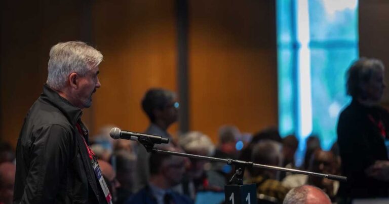 Man in a busy room speaking via a microphone